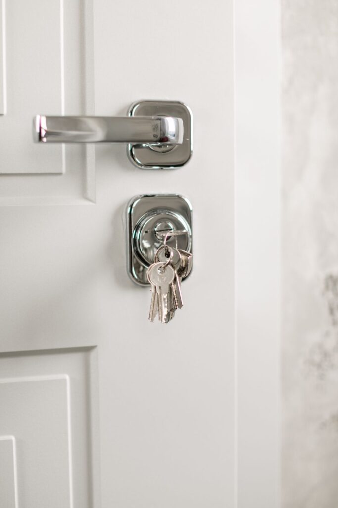 Chrome door handle and keyed cylinder with keys on a white apartment door