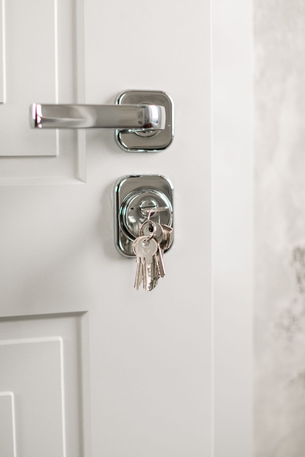 Chrome door handle and keyed cylinder with keys on a white apartment door