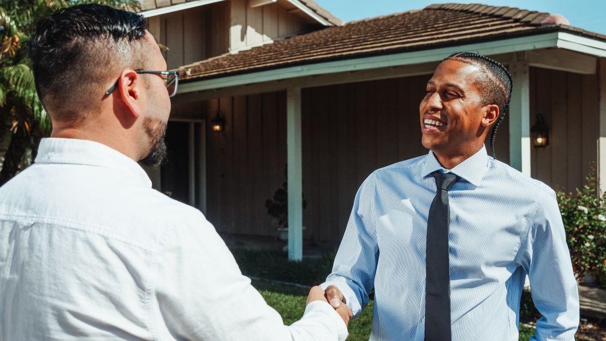 Two men shaking hands outside a house after agreeing on a repair estimate
