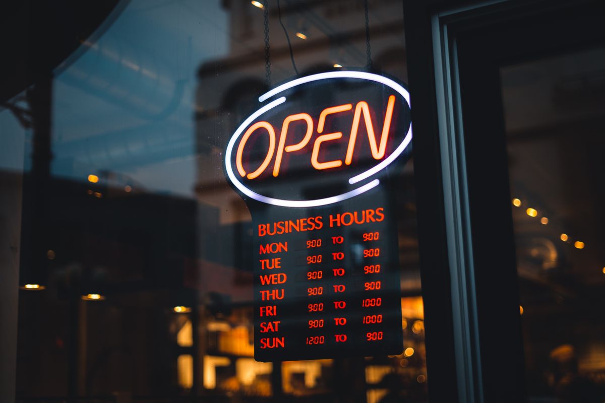 Neon open sign with business hours in a storefront window at night