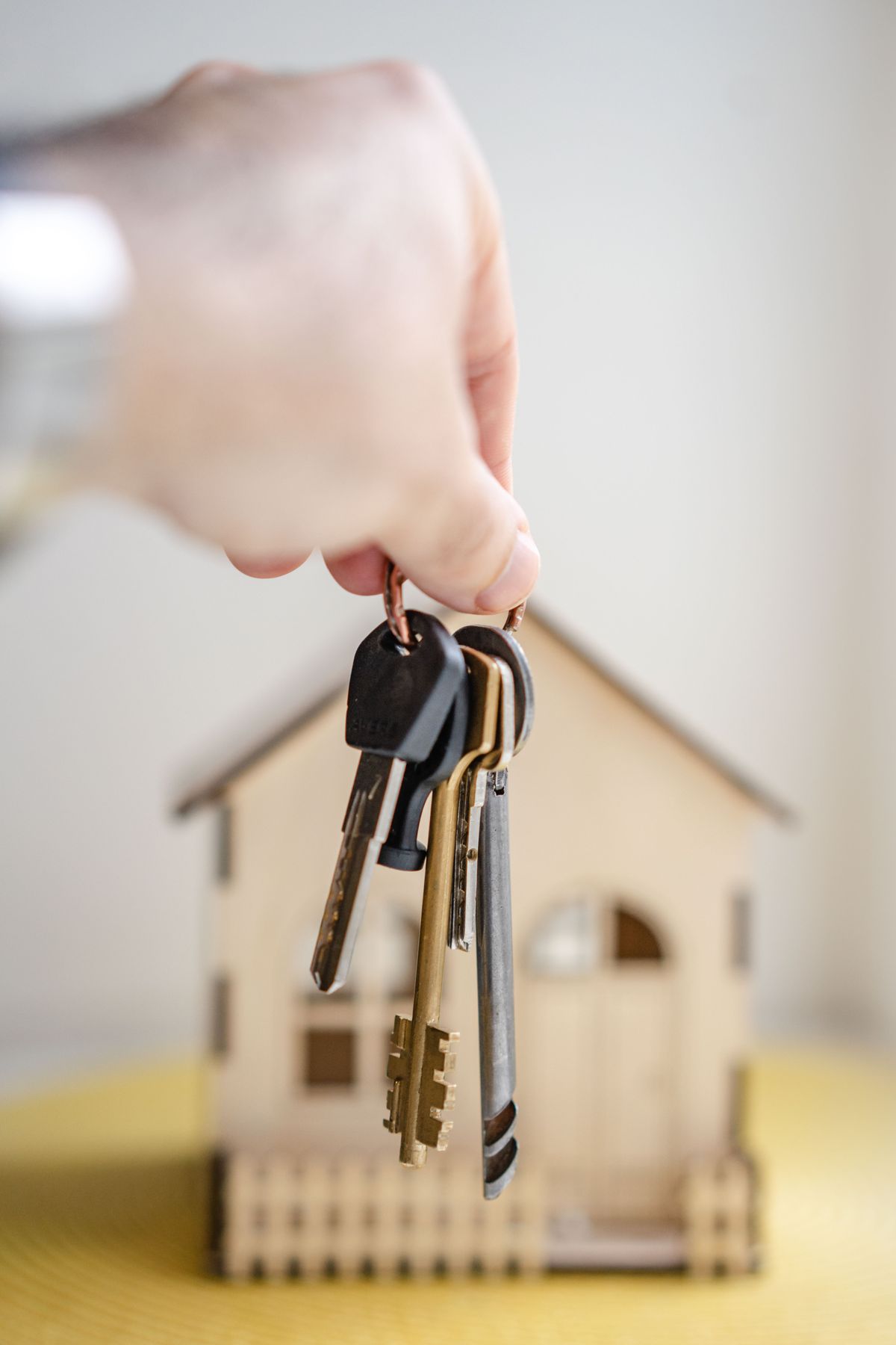 Hand holding a set of keys in front of a small model house
