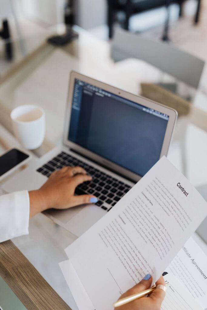 Person reviewing a printed contract while working at a laptop
