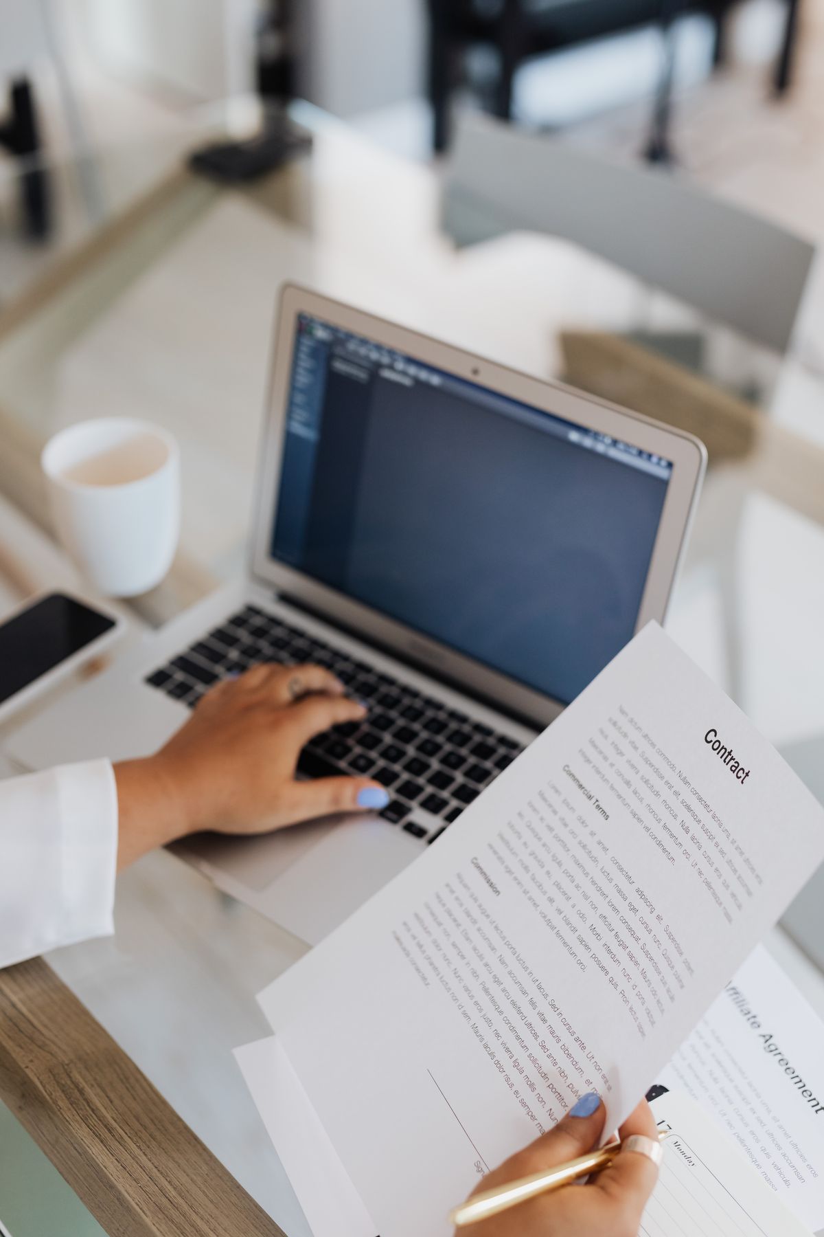 Person reviewing a printed contract while working at a laptop