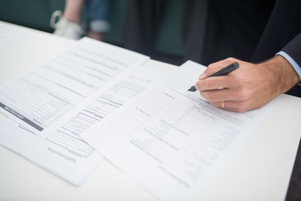 Hand with a pen filling out forms at a desk