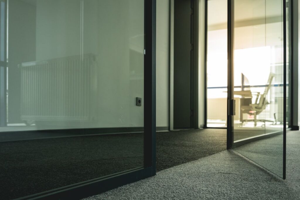 Glass commercial door in a dark aluminum frame, propped open in a modern entryway