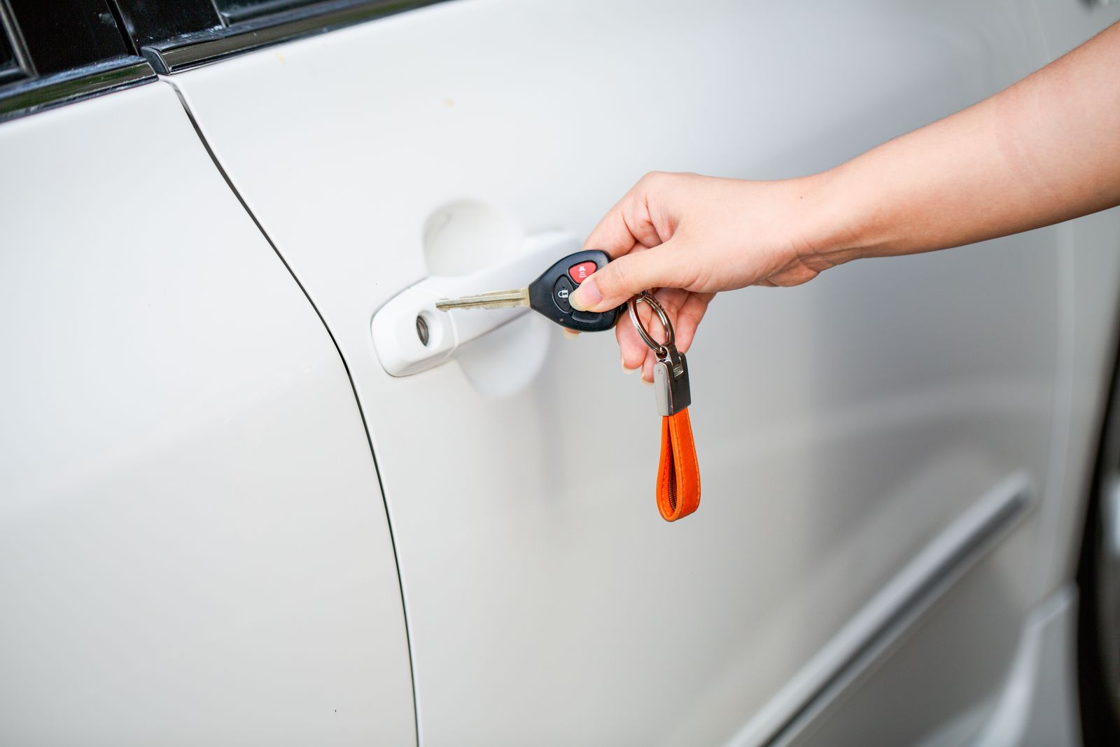 Hand holding a car key with remote head at a car door